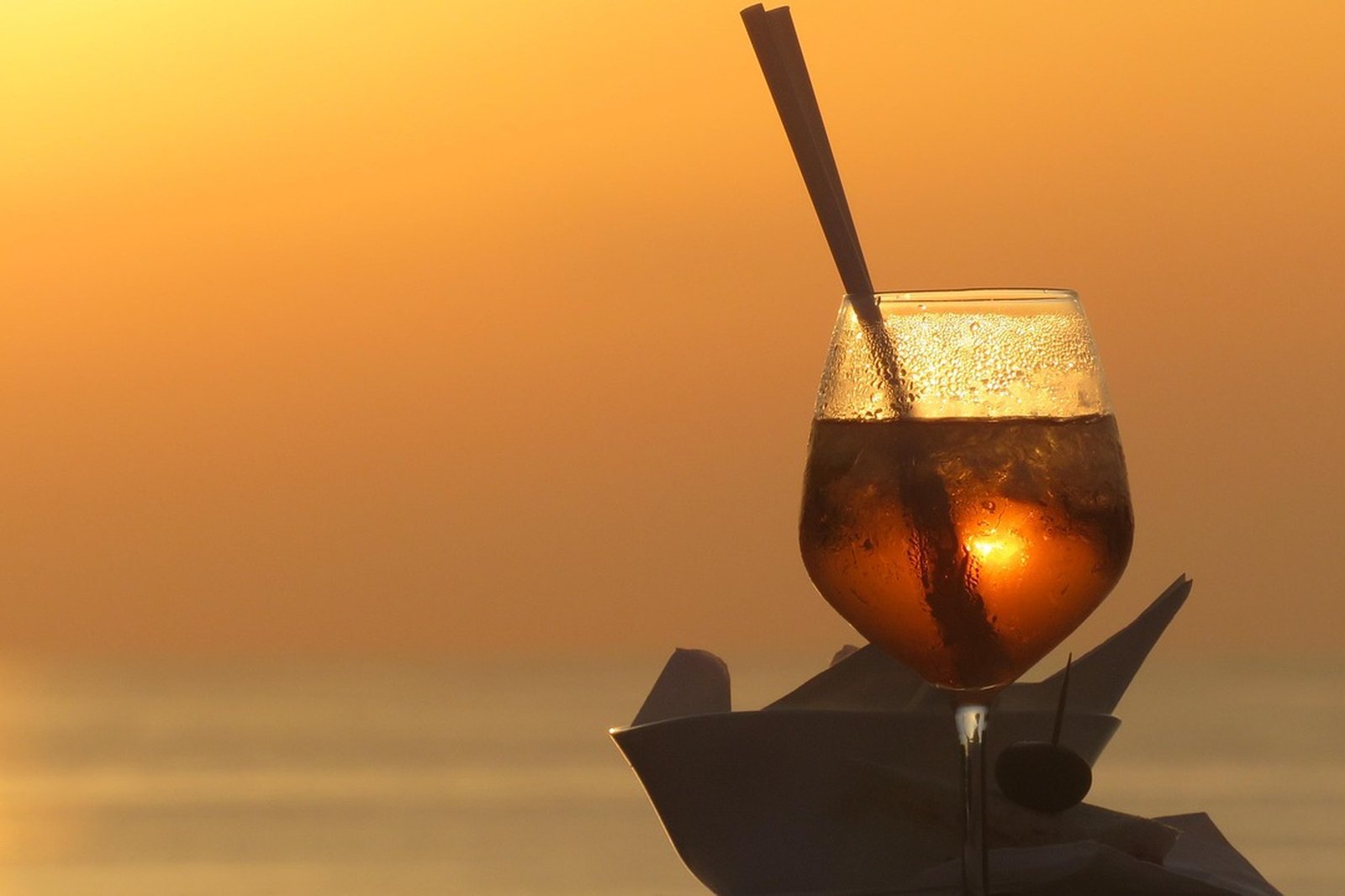 A spritz glass glowing against an orange sunset over the sea